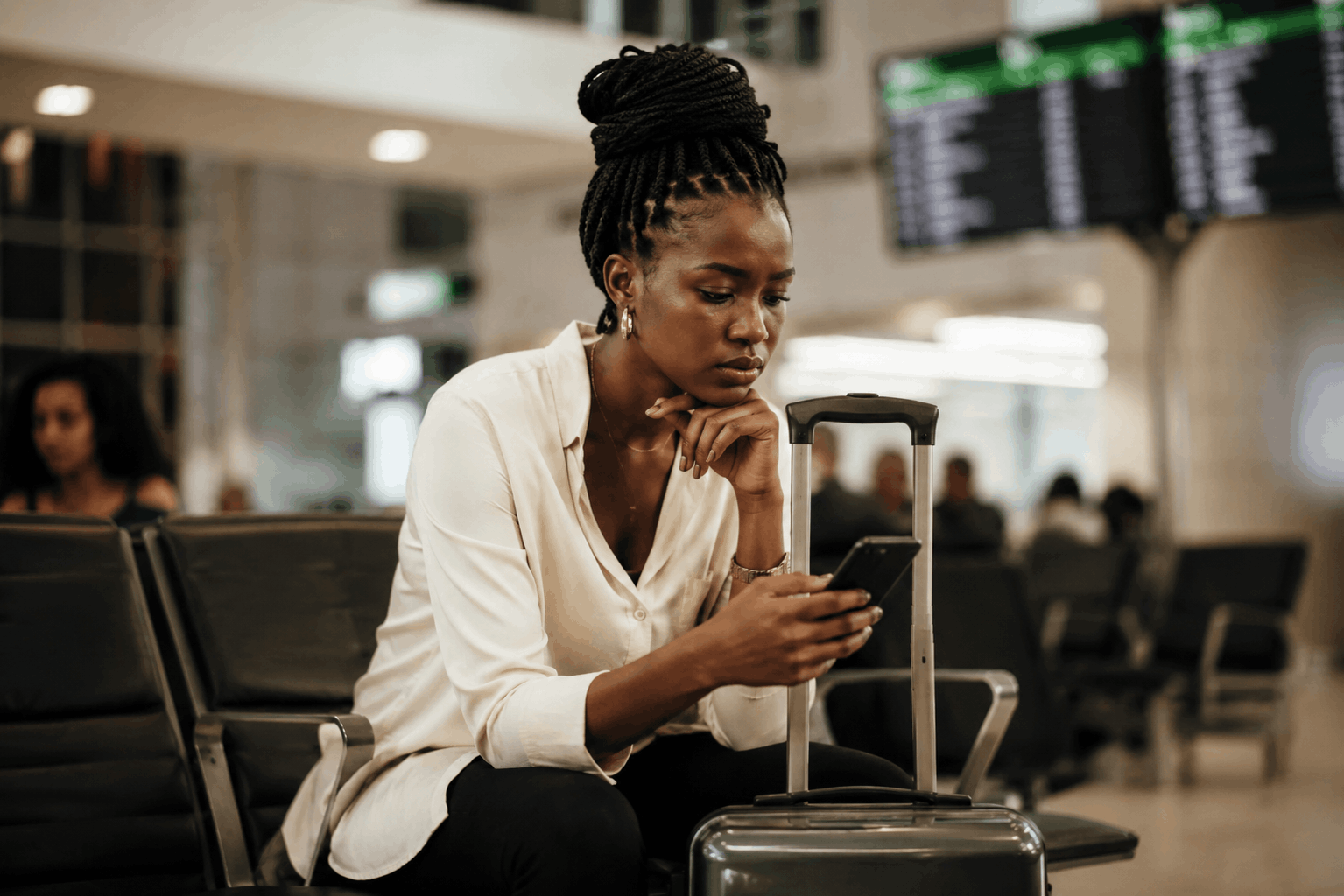 Black woman checking her phone while waiting with luggage in an airport lounge, highlighting Nigeria’s shift from visa on arrival to pre-travel e-visa approval.